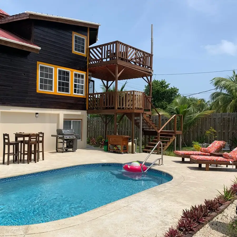 wood three story building, exterior wood stairs, kidney shaped pool, cushion covered wood decks, wood dining table, chairs and grill with floatie in pool