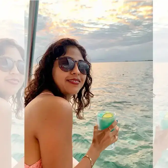 Woman wearing sunglasses enjoying a blue tropical cocktail while seated on a boat during a scenic sunset cruise over the calm waters of Belize.